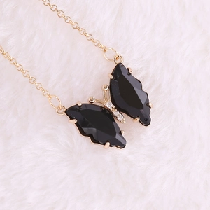 Detail shot of a black faceted butterfly pendant on a gold chain over white faux fur