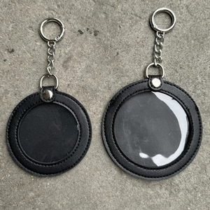 Detail view of two black round leather keychain badge holders with clear window and metal snap