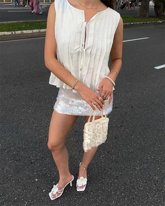 Detailed view of white tie-up sleeveless top and silver sequined mini skirt with sandals