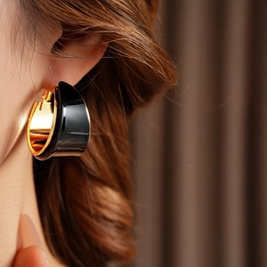 Close-up of model wearing black resin and gold plated C-shaped wide hoop earrings