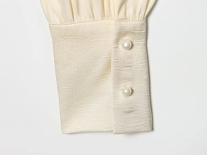 Dettaglio dei polsini in raso beige elegante con doppi bottoni di perla e trama liscia