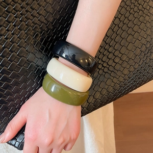 Gros plan détaillé d'un ensemble de trois bracelets en acrylique brillant noir, crème et olive