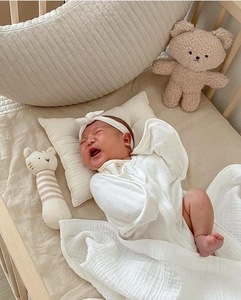 Detail of white cotton muslin swaddle blanket set with matching headband on wooden crib