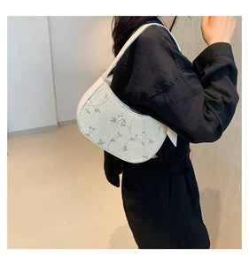 Detail of woven straw shoulder bag featuring delicate green floral embroidery and ivory texture