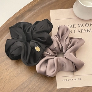 Close-up of premium black and pink satin scrunchies displayed on a dark wooden tray