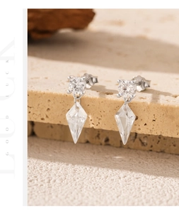 Detailed shot of S925 silver earrings with kite-shaped crystal drops on beige stone