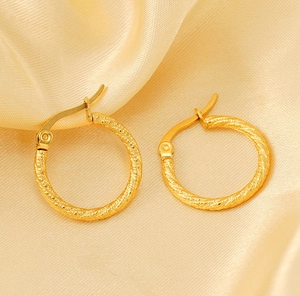 Macro view of gold-plated twisted rope hoop earrings on champagne silk background