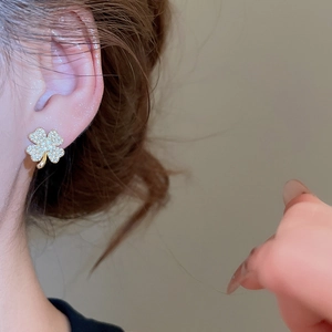 Macro shot of clover shaped gold earrings with sparkling zircon crystals on a model