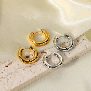 Detailed view of polished thick gold and silver hoop earrings on elegant silk and stone