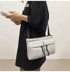 Detail shot of white nylon messenger bag with double front pockets and side logo tag