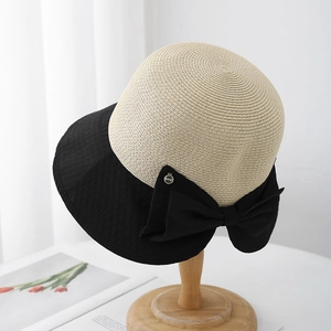 Detail of elegant straw sun hat featuring a large black bow and metallic brand charm