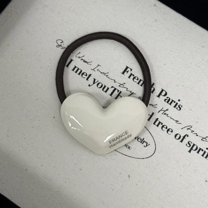 Detail of a white heart-shaped hair tie with FRANCE Handmade text on a beige fabric base