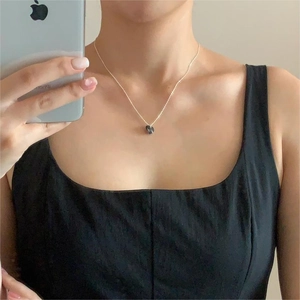 Close-up of a minimalist silver S925 necklace with a dark round charm worn by a model