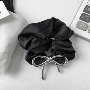 Detail of black satin hair tie featuring a glossy silver metal bow on white background