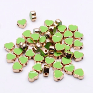 Close-up of heart-shaped light green enamel beads with rose gold edges for DIY jewelry