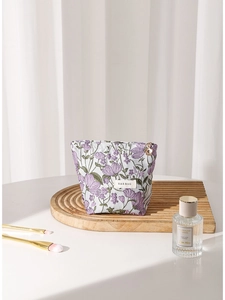 Purple floral embroidered canvas cosmetic bag with metal zipper on a wooden tray