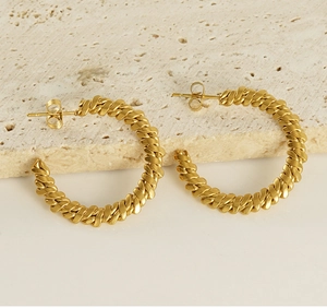 Detailed close-up of 18K gold-plated twisted rope hoop earrings on a natural stone surface