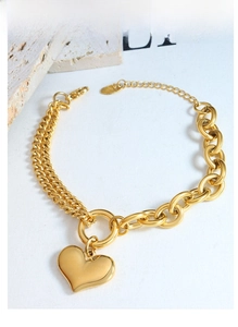 Detail of 18K gold-plated Cuban link chain bracelet with a heart pendant macro view