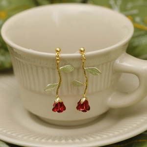 French luxury rose drop earrings with red enamel buds and gold metal stems on a cup