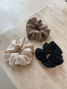 Detail view of rhinestone scrunchies in cream, brown, and black on a stone surface