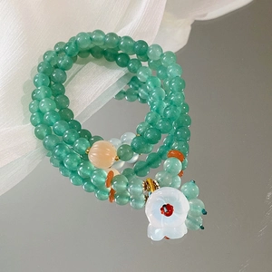 Detail eines dreilagigen Perlenarmbands mit grünen Jadeperlen und Blumenanhänger