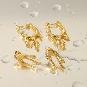 Macro shot of gold-plated lava teardrop earrings with elegant pearls on a mirror surface