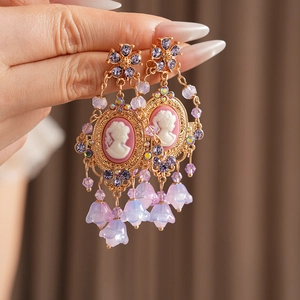 Close-up of vintage gold earrings with cameo portraits and purple flower tassels