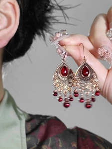 Detail of bohemian teardrop earrings featuring ruby red stones and bronze tassels