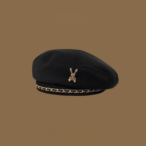 Classic black beret with golden rabbit charm and decorative chain detail on brown background