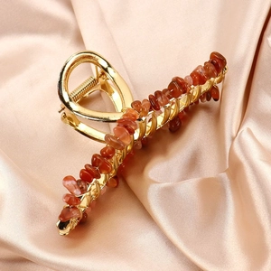Detail of red carnelian stones woven on a large golden metal hair claw clip over silk
