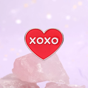 Broche cœur émaillée rouge avec texte XOXO sur pierre rose et fond violet élégant