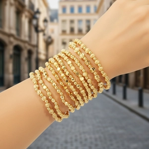 Layered gold bead bracelet set with irregular geometric charms and elastic wristband