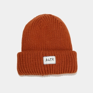Close-up of thick ribbed knit caramel beanie featuring a white rectangular AQER logo tag