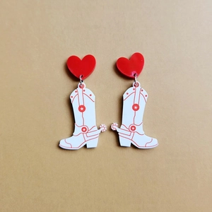 Detailed shot of red acrylic heart studs and patterned cowboy boot dangling earrings