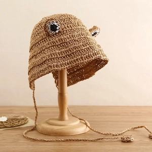 Close-up of brown straw hat with cute frog eyes design and woven strap details