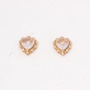 Macro shot of gold heart pendants with clear zircon stones on a water drop background