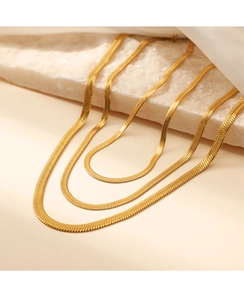 Detail of layered gold snake chain necklace on textured stone base for fashion styling