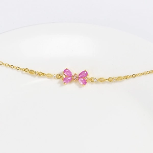 Macro view of a gold chain bracelet with a pink butterfly crystal pendant on a white plate