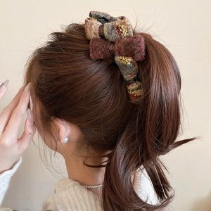 Detail view of a tweed textured velvet bow hair claw clip in warm coffee and beige tones