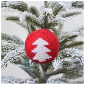 Macro detail of red wool felt Christmas ball with white tree pattern on snowy branch