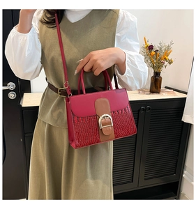 Detail showing contrast textures of a burgundy crossbody bag with gold buckle on a model