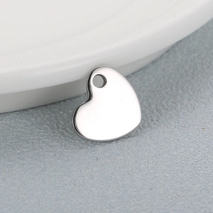 Polished silver heart pendant in stainless steel on a white ceramic plate
