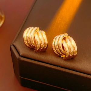 Close-up of golden geometric twisted hoop earrings on a textured brown surface