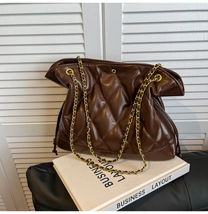 Detail of a brown quilted bucket bag with golden chain strap and smooth leather texture