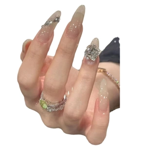 Long transparent press-on nails with large rhinestones and a green gemstone ring