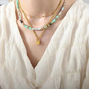Detail of layered gold necklaces with colorful beads and a polished square lock pendant
