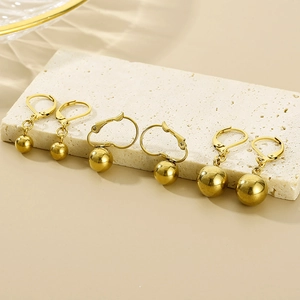Detailed close-up of golden spherical drop earrings displayed on a textured stone stand
