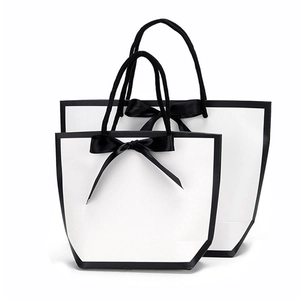 Minimalist white gift paper bags with black trim, ribbon bow, and rope handles in two sizes