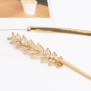 Detail of a gold metal elastic belt featuring a decorative leaf buckle on white backdrop