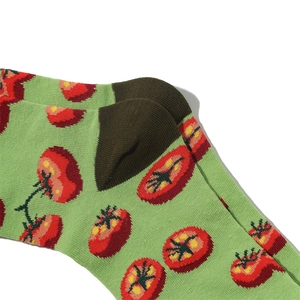 Close-up of green cotton socks featuring red tomato patterns and knit texture detail